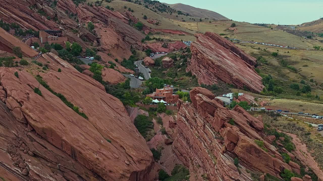 Drone aerial orbits Red Rocks Amphitheatre showing striking red cliffs and desert vegetation under clear light