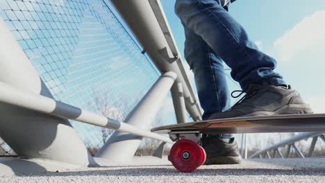 Close-up-view-of-a-person’s-feet-standing-on-a-skateboard-near-a-metallic-fence-under-a-clear-sky