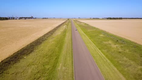 Carretera-De-Campo-Con-Vehículo-Conduciendo-A-Través-De-Un-Exuberante-Campo-De-Trigo-En-Verano---Toma-Aérea-De-Drones