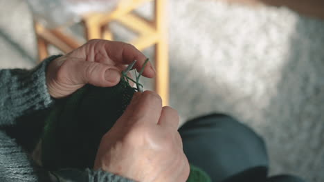 the hands of an unrecognizable woman knitting with green wool