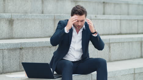 upset businessman reading bad news on laptop screen at urban street