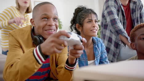 Happy-diverse-group-of-teenage-friends-sitting-on-couch-and-playing-video-games-at-home,-slow-motion