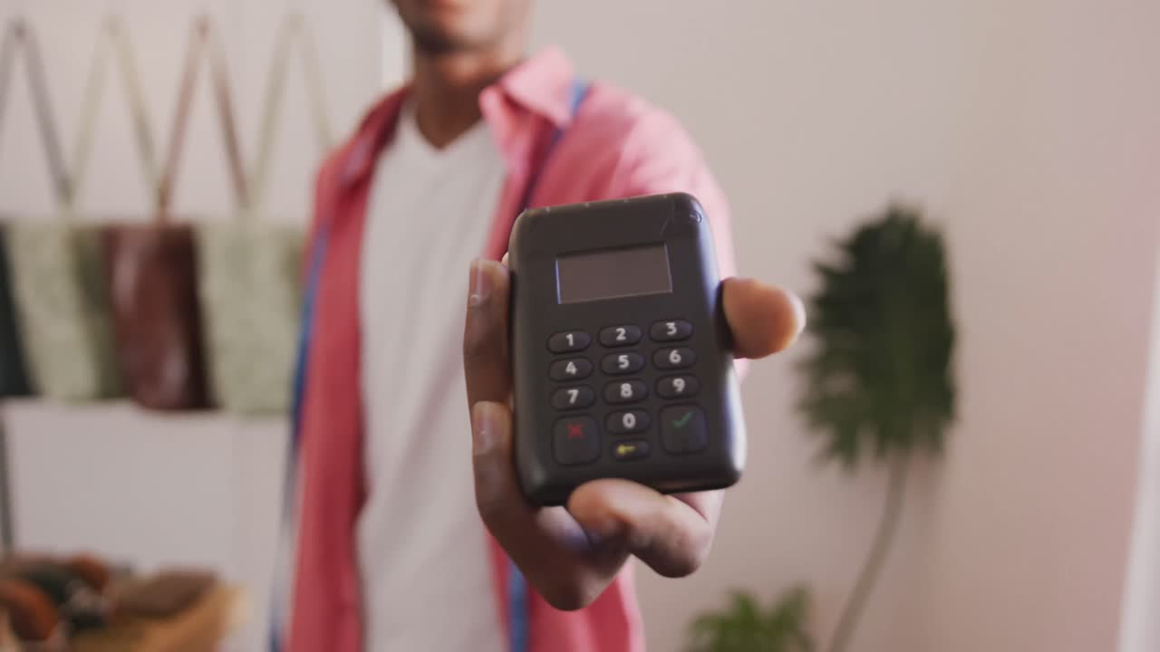 Hand of african american craftsman holding payment terminal in leather workshop