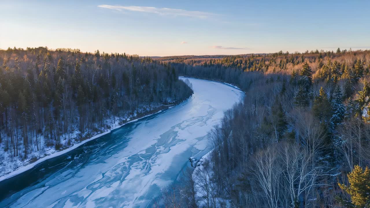 Drooni seuraa eteenpäin vetäen jäätynyttä jokea lumipeitteisen metsän läpi, auringon valaisemat jäälevyt kimaltelevat