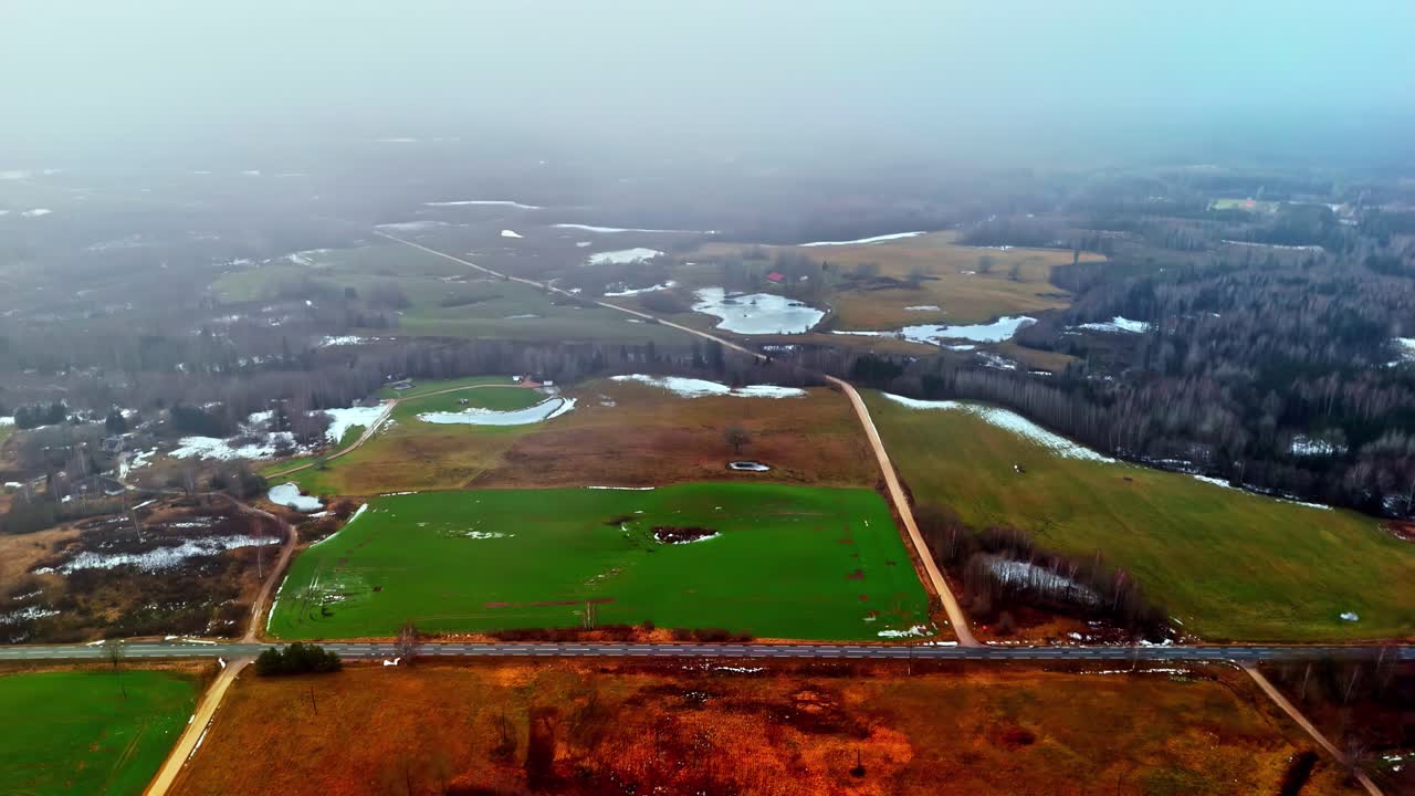 Luftfoto av tåkete landskap på landsbygda med smeltende snø og grønne jorder.