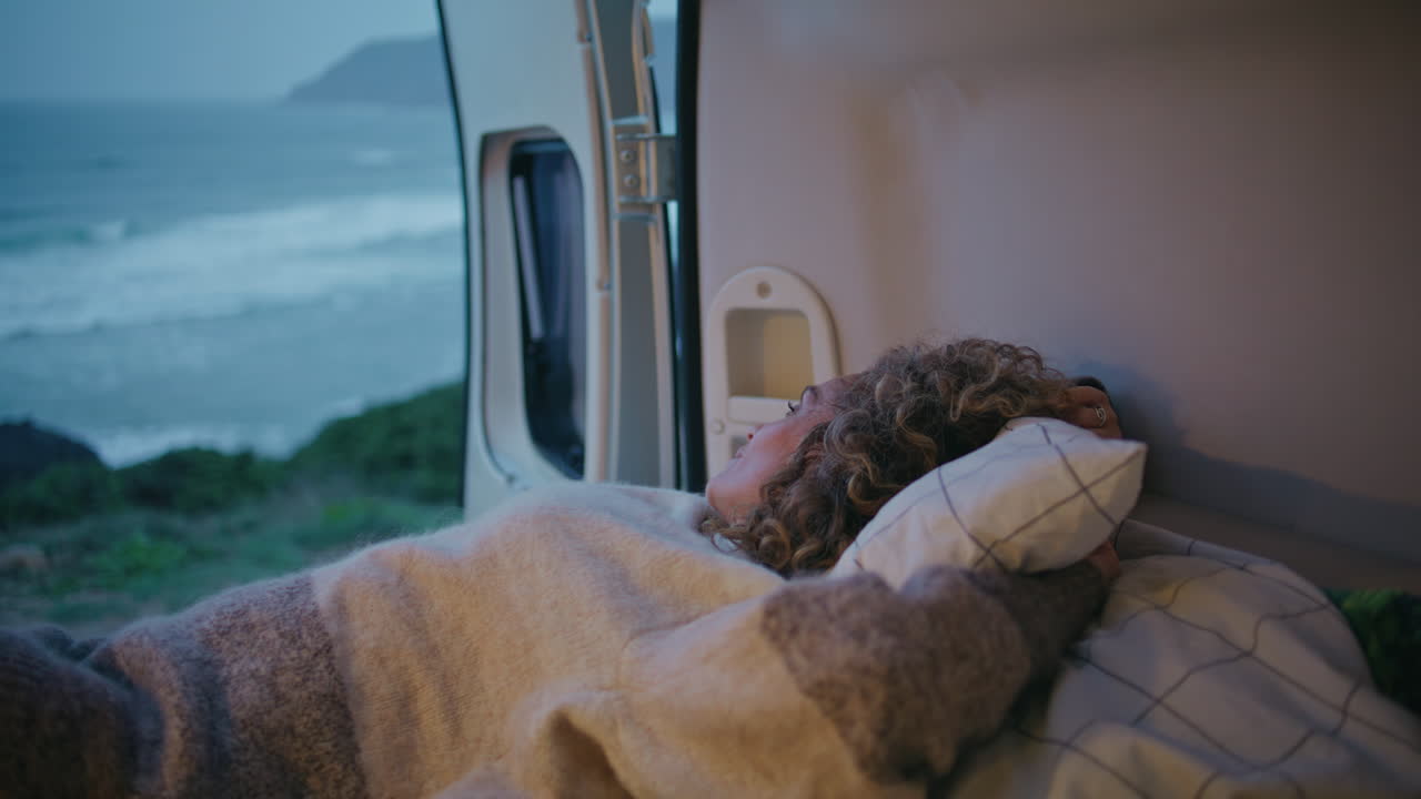 el viajero del campamento descansa en la cama del remolque de la furgoneta mirando el paisaje marítimo sombrío de cerca.