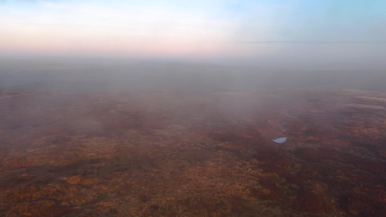 Aerial flight through dense clouds covering heather and moor of Kinder Scout Mountain