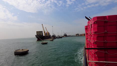 ferry sailing away from the port of banjul in gambia, with view of docked shipping vessel in daytime