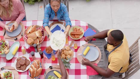 happy diverse group of friends eating and talking at dinner table in garden, slow motion