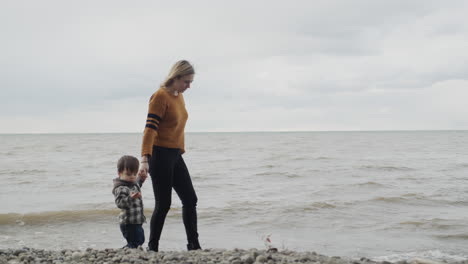 a young woman leads a boy by the hands along the rocky seashore