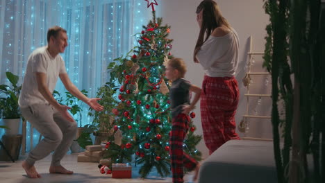 Mamá-E-Hijo-Decoran-El-árbol-De-Navidad-En-La-Sala-De-Su-Casa-Y-Se-Abrazan-Todos-Junto-A-Su-Padre-Después-De-Completar-El-Escenario.-Familia-Feliz-En-Pijama-En-Víspera-De-Navidad.-Imágenes-4k-De-Alta-Calidad