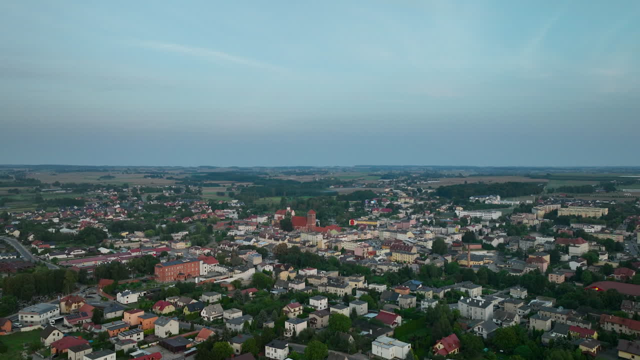 vista aérea de una pequeña ciudad al anochecer, con una iglesia en el centro, rodeada de áreas residenciales y campos abiertos - ciudad de lubawa