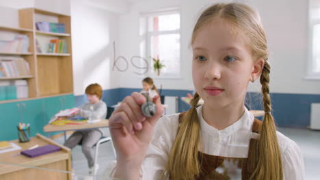 niña bonita en el aula escribiendo colores en inglés en un tablero de vidrio en la escuela