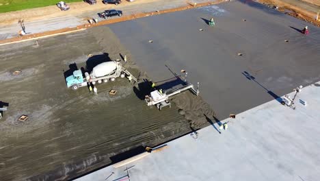 a concrete mixing truck begins to pour its load while workers manage the concrete spout