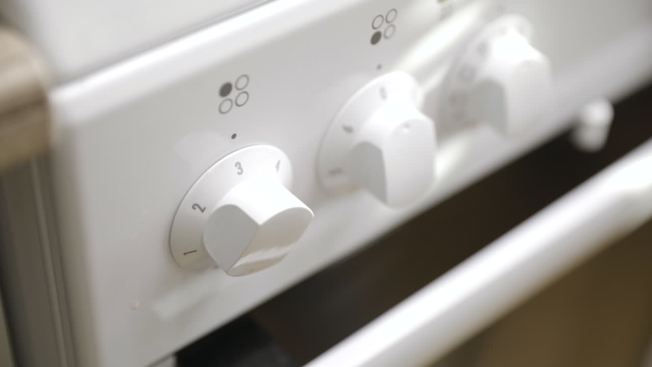 Close-up of young male hand turning plate on stove to level three heat