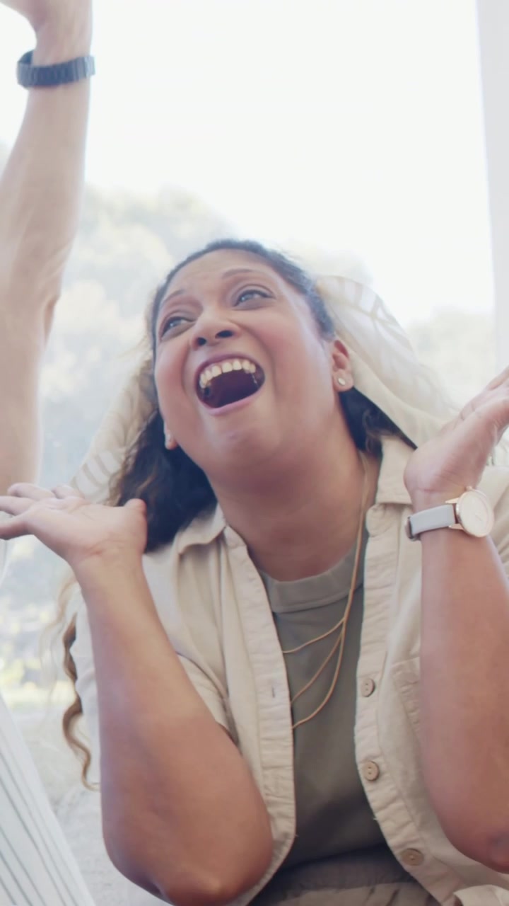 Vertical video: Reacting to off-screen reveal, woman clapping and laughing on sofa by mountain view