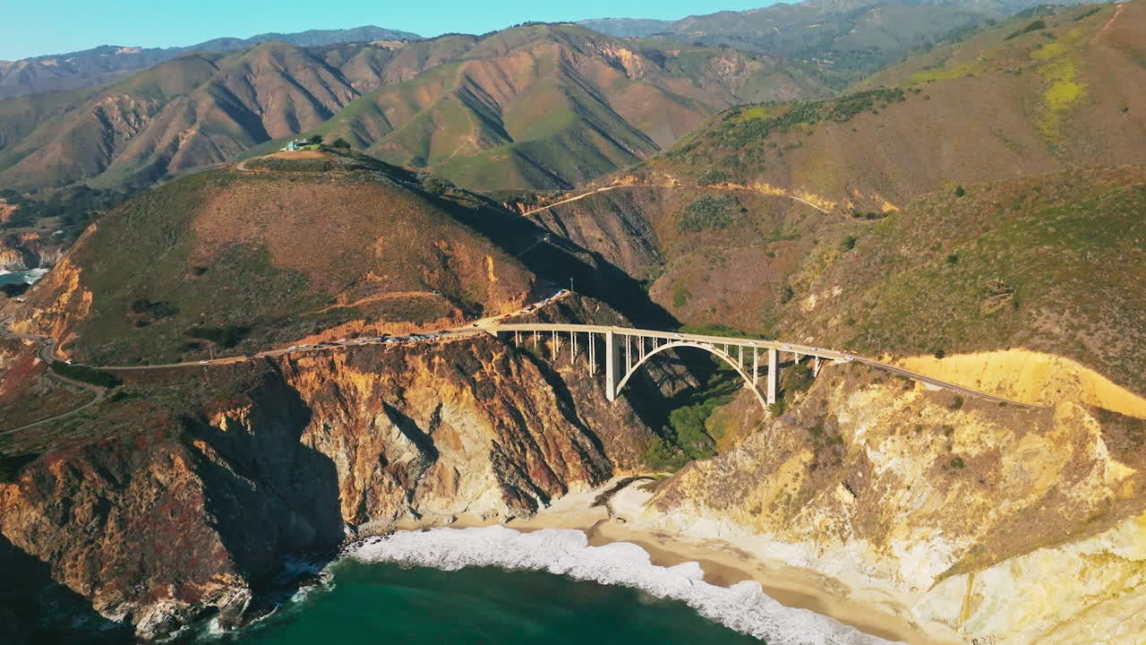 Splendid panorama of California mountains with bridge at the foot. Little sandy beach with white waves slowly arriving to. Aerial view.