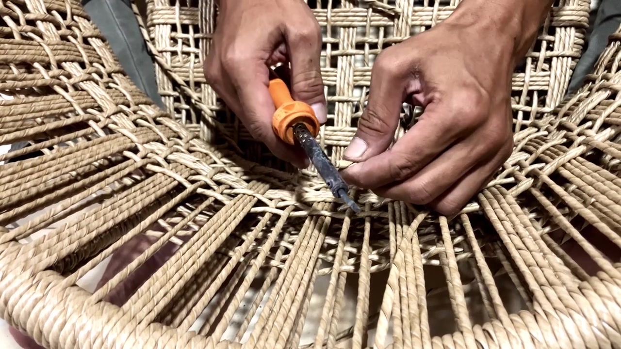 Slow motion close-up shot of artisan hands weaving natural fiber cord to create a traditional chair seat. Detailed view of the craftsmanship and handmade furniture making process.