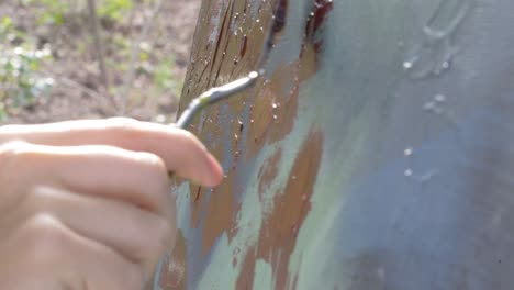 female artist smearing red paint and creating texture on multicolored abstract painting outside during the day, camera tilt down