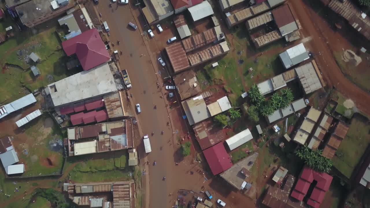 Overhead drone view of Kapchorwa Town showing scattered traffic along Kapchorwa–Suam Road, flanked by buildings and red earth terrain in Uganda's eastern highland region.