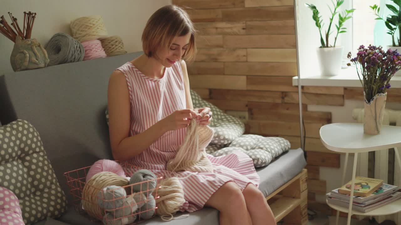 집 작업장에서 소파에 앉아 양털 스웨터를 뜨는 미소 짓는 여자