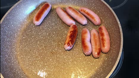 overhead shot of flipping cooking sausage on frying pan