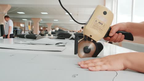 female worker on a sewing manufacture uses electric cutting fabric machine. sewing production line