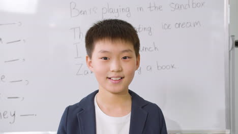 student standing in front of blackboard in english classroom smiling and looking at camera