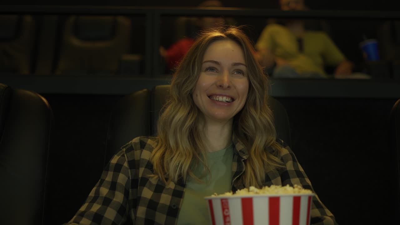 Donna allegra che guarda una commedia al cinema, mangiando popcorn.
