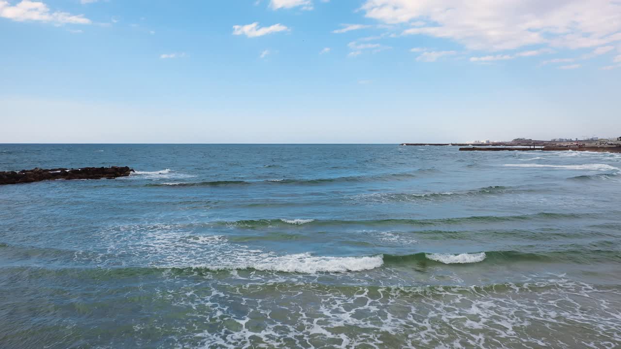 부드러운 파도가 날아다니는 지중해와 푸른 하늘은 화창한 날 공중에서 모래 위를 걷고 있는 젊고 매력적인 낭만적인 커플을 드러냅니다.