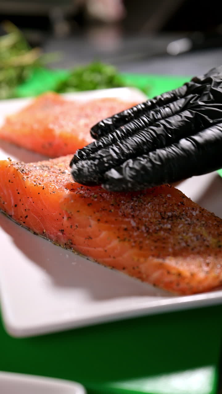 Chef preparing salmon fillets with seasoning. Close-up of salmon fillets being prepared with spices by a chef wearing black gloves