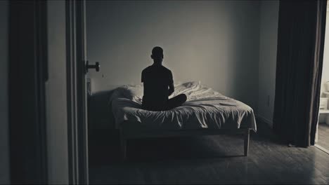 silhouetted male figure sitting pensively on bed, casting deep shadow against dim room, embodying inner struggle and profound emotional landscape of human introspection