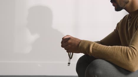 1 뒤에 있는 벽에 그림자를 드리우고 있는 염주를 들고 기도하는 이슬람 남자의 클로즈업