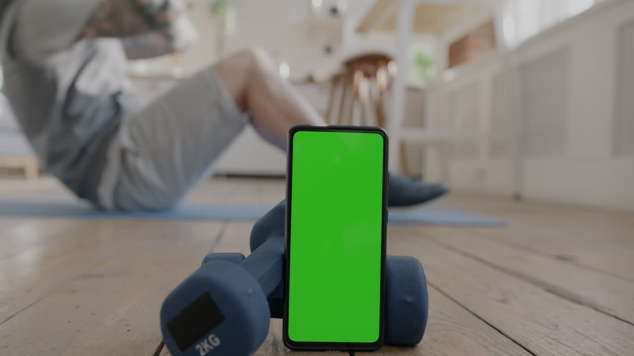 Man Doing Sit-Ups at Home with Smartphone and Dumbbells