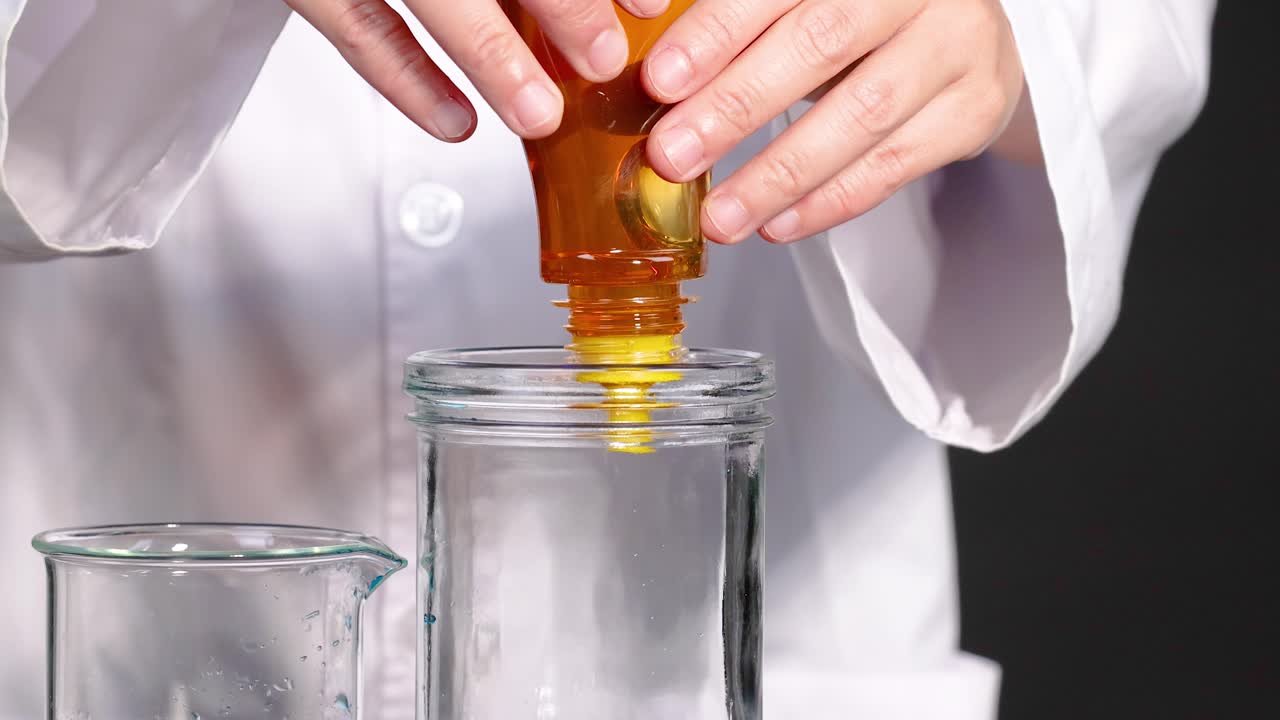 실험실 코트를 입은 사람이 과학적 실험을 보여주는 파란 액체가 들어있는 항아리에 을 부어줍니다.