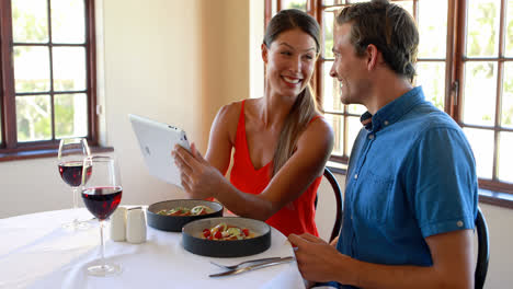 pareja sonriente usando una tableta digital en un restaurante
