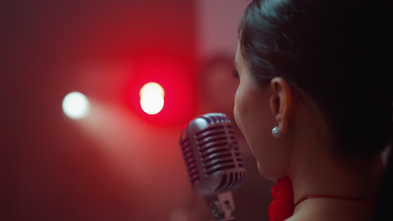 Close-up of a passionate female singer from the back, singing into a vintage microphone with a blurred red background