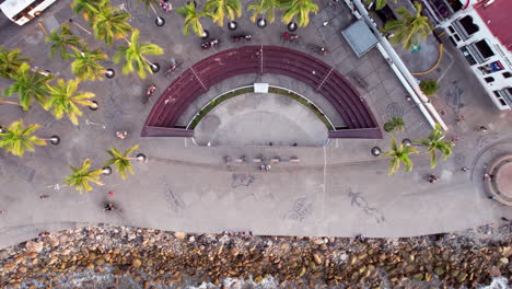 Aerial-video-featuring-a-zenithal-view-of-the-boardwalk-at-the-arches-of-Puerto-Vallarta,-capturing-the-outdoor-theater-by-the-sea-as-well