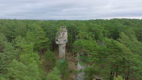 Establishing-aerial-view-of-old-Soviet-military-concrete-observation-watchtower,-pine-tree-forest,-Liepaja-,-military-heritage,-Nordic-woodland,-wide-drone-shot-moving-forward
