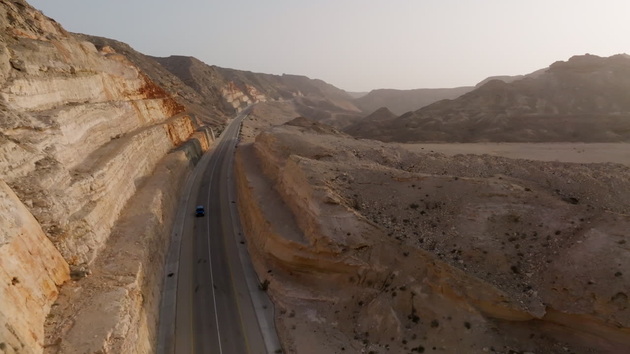 Winding road along desert cliffs in Oman, with a car driving peacefully