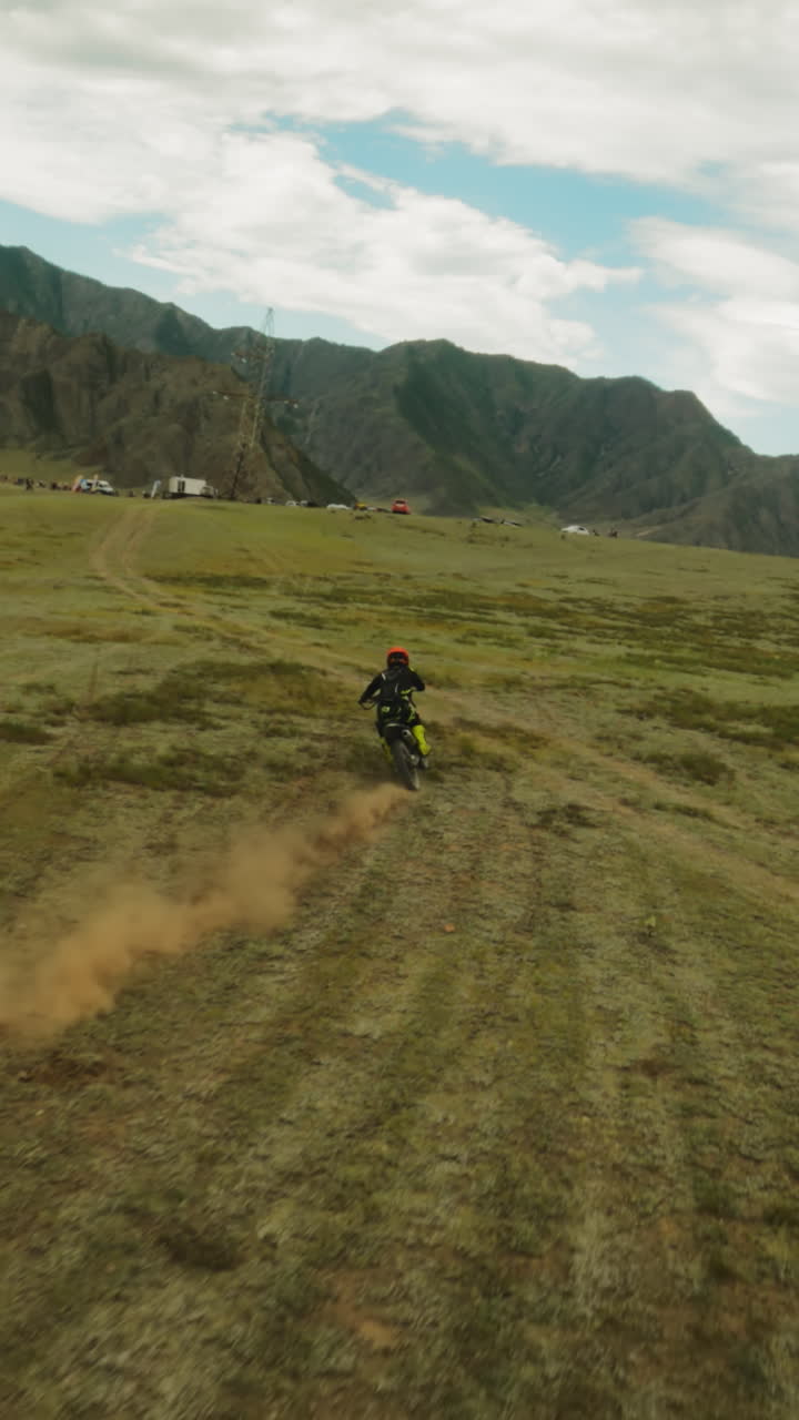 persona monta en motocicleta a lo largo del valle de la montaña fpv. deportista en motocicleta cruza el área offroad con el campamento de entrenamiento. libertad y poder de la naturaleza