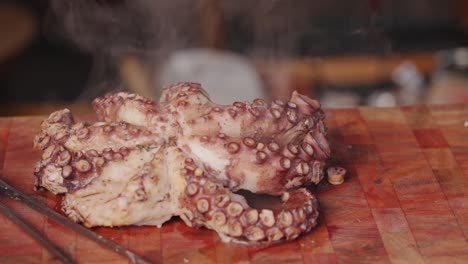 Filmische-Food-Videografie,-Kamerafahrt-Eines-Frisch-Gekochten-Oktopus-Auf-Einem-Schneidebrett,-Während-Dampfend-Heißer-Wasserdampf-Langsam-Von-Der-Oberfläche-Verdampft