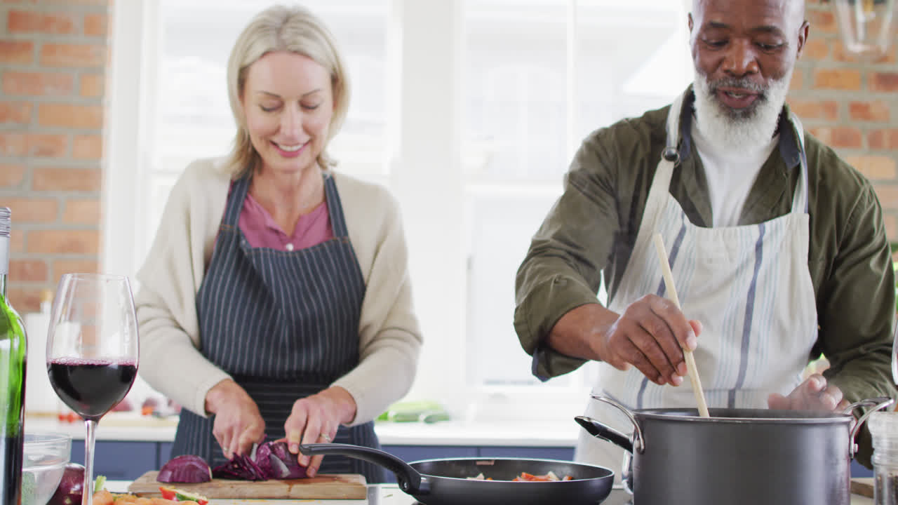 pareja de alto nivel de raza mixta con delantales cocinando juntos en la cocina en casa
