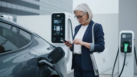woman using smartphone while charging her electric car at an ev station