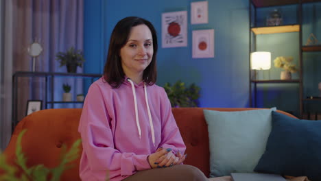 Portrait-of-young-happy-woman-sitting-on-sofa-at-home-looking-at-camera-and-smiling-in-positive-mood