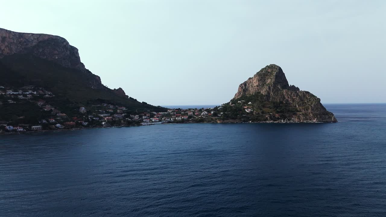 Aerial 4K footage of Capo Zafferano and Sant Elia on the Sicilian coast showing dramatic rocky headland deep blue sea and hillside houses near Porticello and Bagheria in evening light