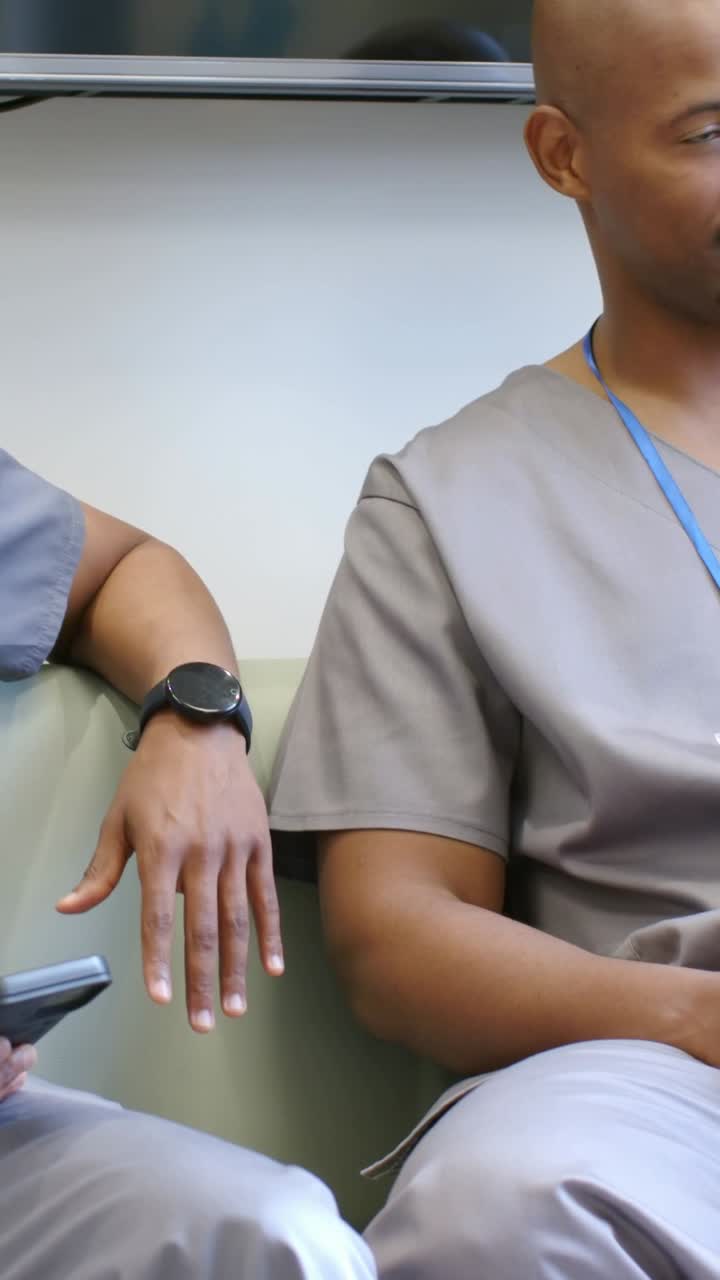 Video verticale: uomo in camice che controlla il telefono, seduto su un divano in clinica, gesticola e racconta novità, tazza