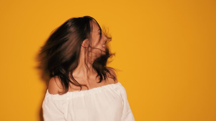Donna con i capelli al vento, top bianco, su sfondo giallo