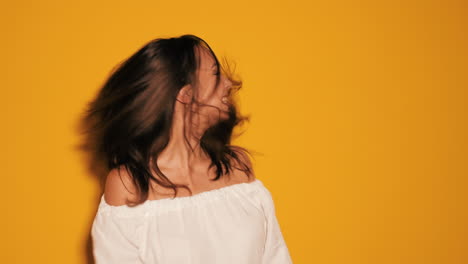 mujer con el cabello en movimiento en la parte superior blanca contra un fondo amarillo