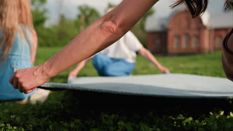women holding blanket from both sides spreading it on grass, preparing picnic area in park, sunlit afternoon, cooperative gesture, green background, casual outdoor leisure
